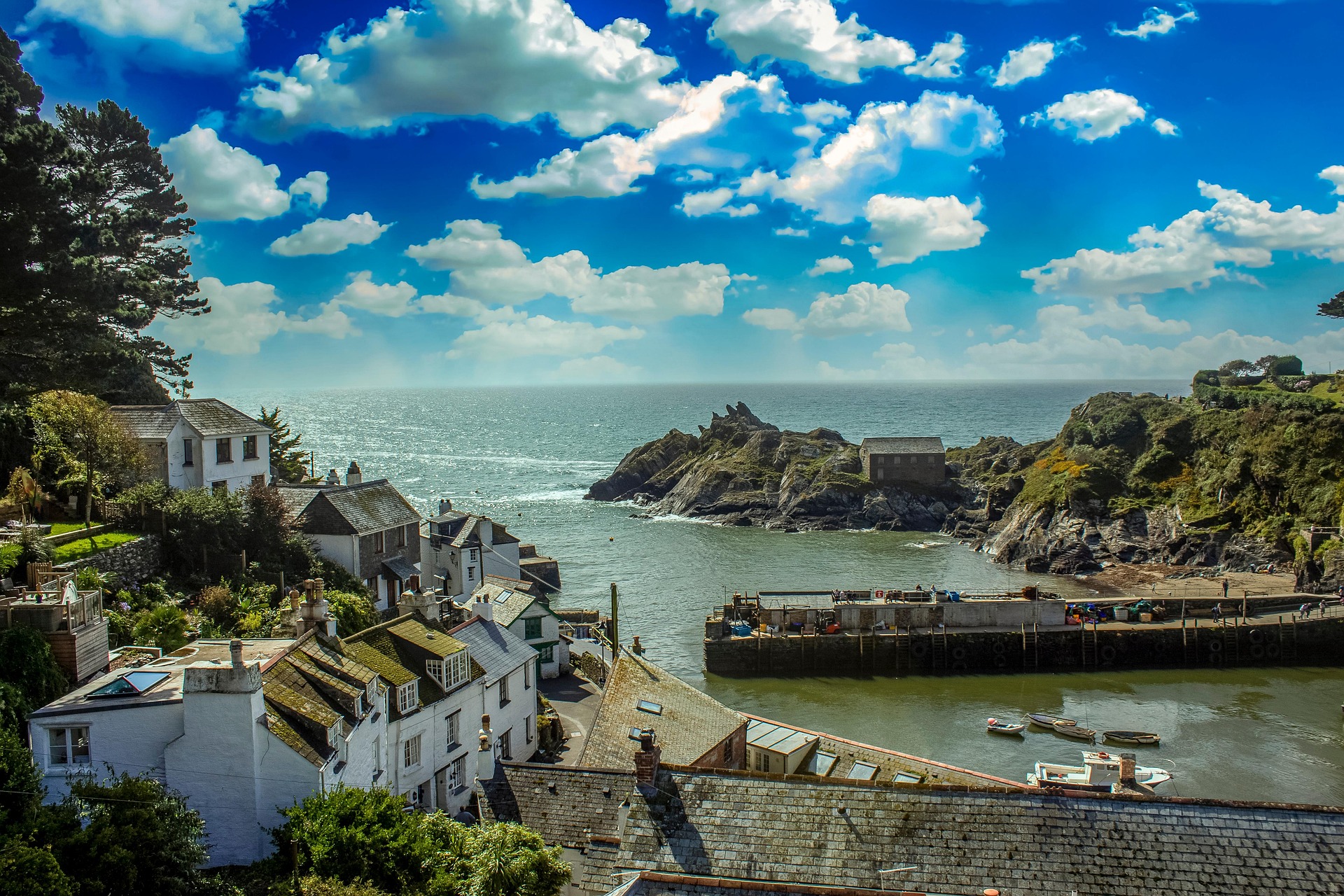 Coastal properties and green landscaping overlooking a Cornish harbour during dry summer weather.
